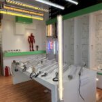 Lighting showroom display featuring industrial tri-proof LED tubular lights, caution-themed hanging tubes, clear PC tube samples on workbench, and various architectural lighting fixtures