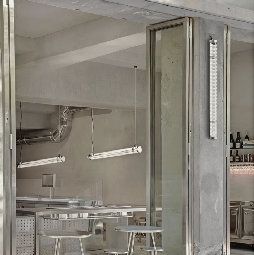 Architectural tubular wall light installed in industrial-style interior with concrete walls and glass partitions