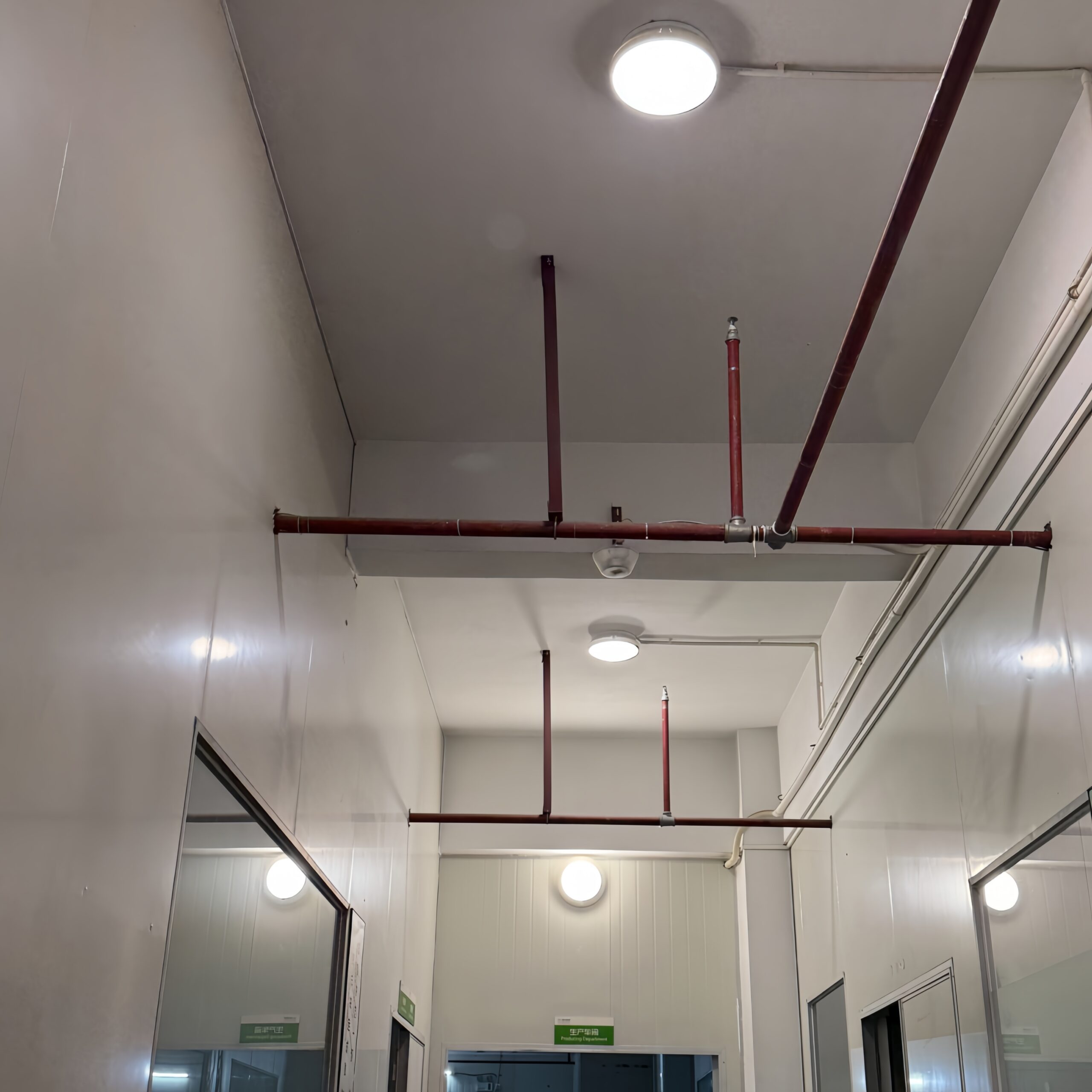 IP65 LED ceiling lights installed in industrial service corridor with exposed piping, providing durable and reliable lighting for technical areas