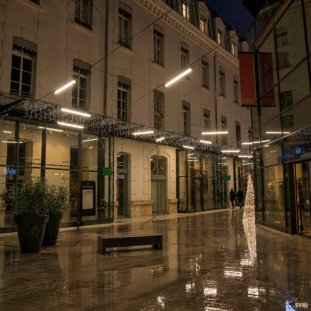 Nighttime outdoor courtyard with suspended tubular LED lights providing warm architectural lighting for pedestrian areas.